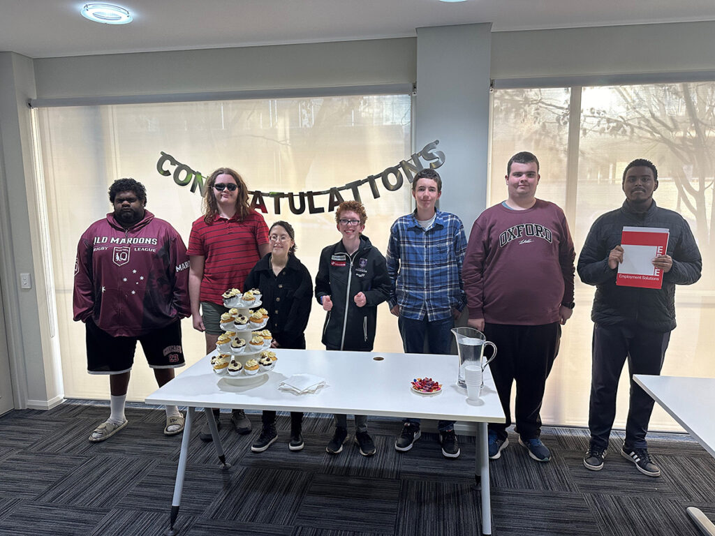 A group of students standing behind a table with a cupcake tower. A sign reading 'congratulations' hangs behind them."