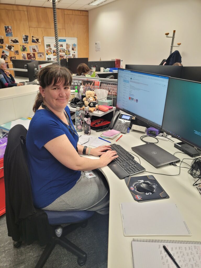 Rachael sitting at her desk smiling while she has our laptop open in front of her.