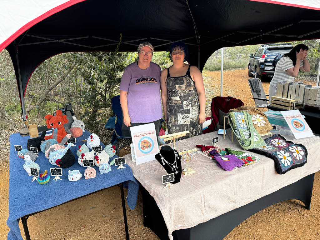 Amelia and her mum standing behind a desk with their crocheted items displayed at the markets.