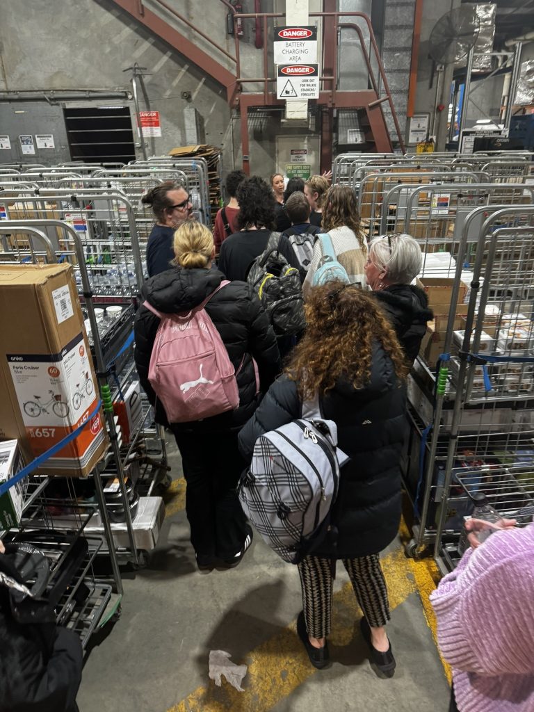 Group of students walking amongst a number of trolleys. Some students are wearing backpacks.