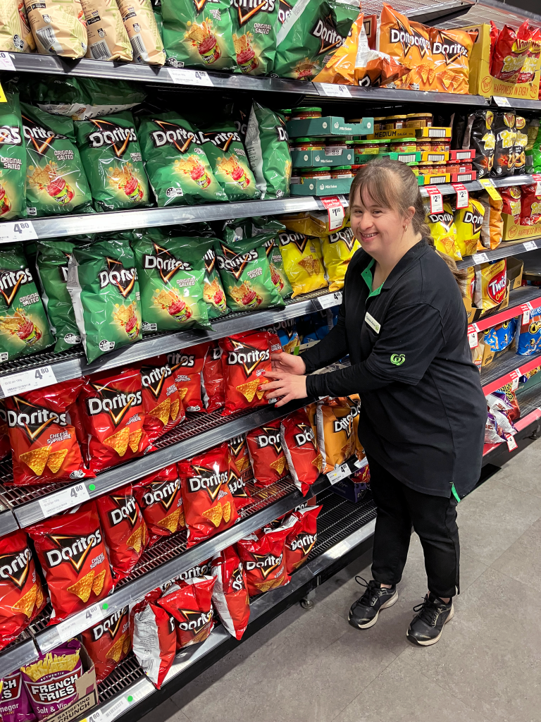 Cassie standing in the chip isle at Woolworths smiling while she grabs a packet of chips.